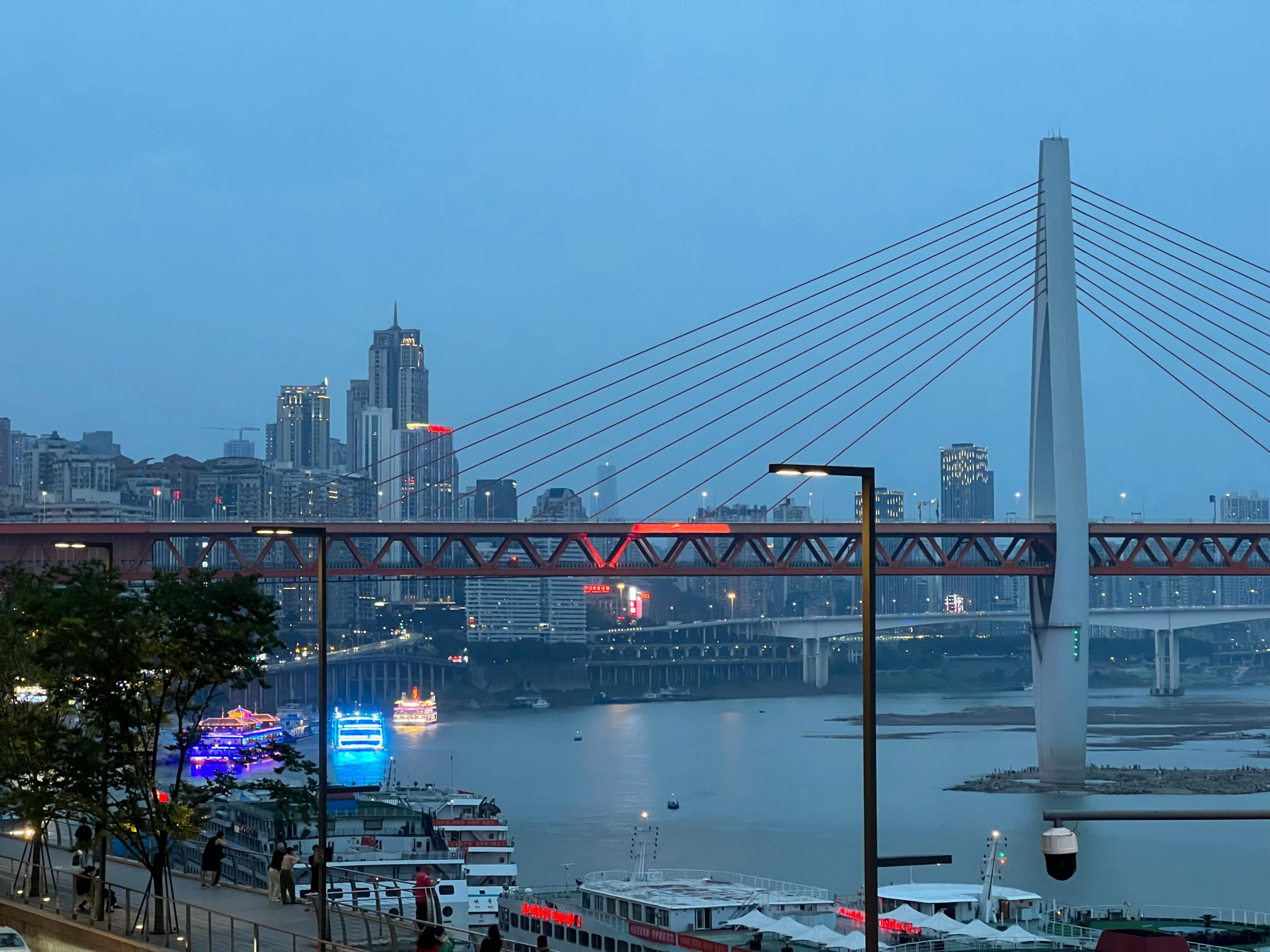 Aerial view of Chongqing at dusk with Qiansimen Bridge and illuminated skyline.